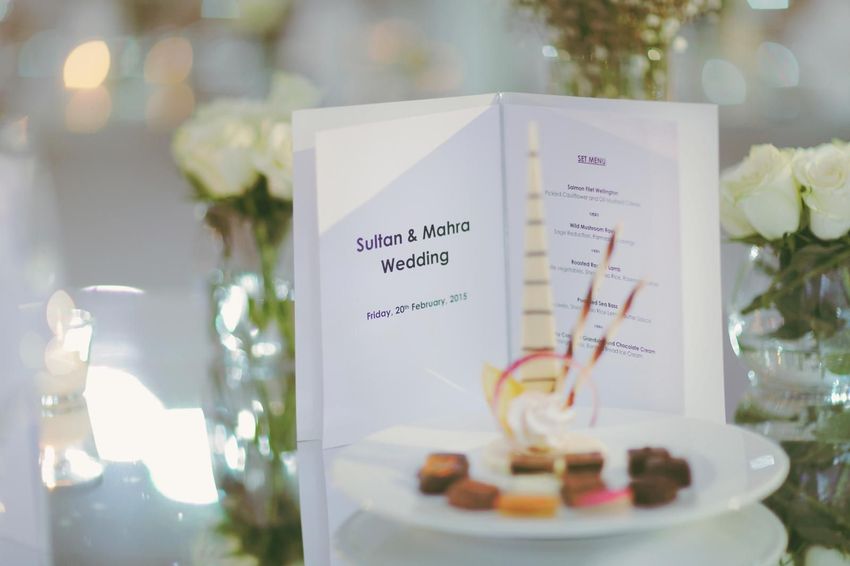 Artisinal chocolates surrounded by individual floral arrangements and wedding program on mirrored table