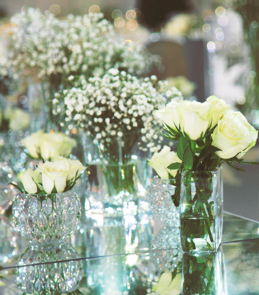 Mini floral arrangements full of white roses and baby's breath flowers in crystal vases