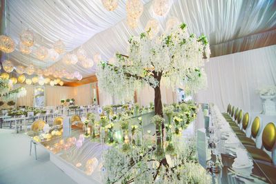 White tented reception with hanging orbs and floral tree accents and mirrored tables and King Louis golden chairs 