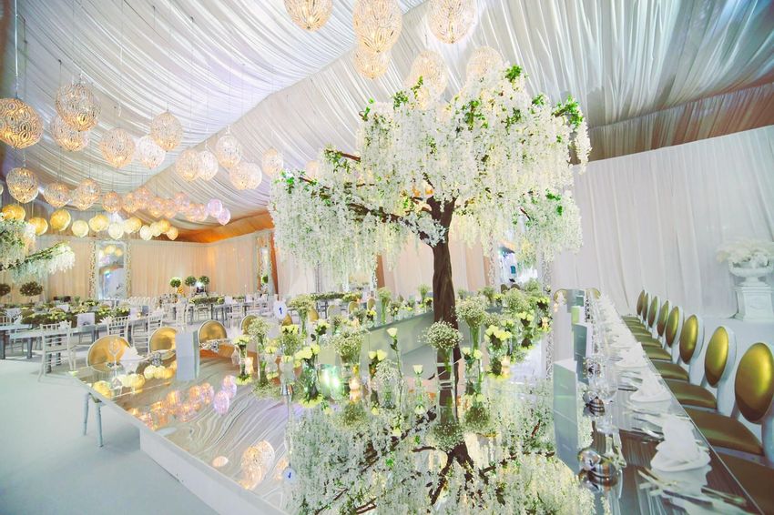 White tented reception with hanging orbs and floral tree accents and mirrored tables and King Louis golden chairs
