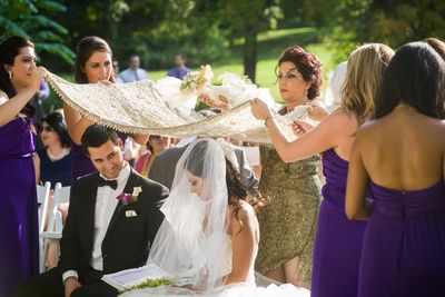 The couple at their Persian sofreh aghd under the traditional shawl held over the bride and bridegroom's head at the Philbrook Museum of Art in Oklahoma