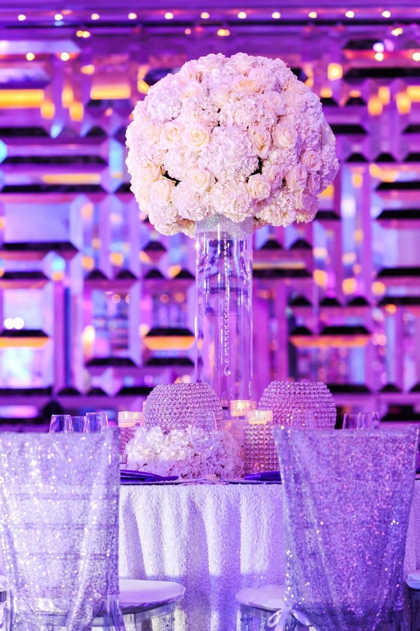 Round dinner tables and ghost chiavari chairs with tall glass vases full of hydrangea and roses 